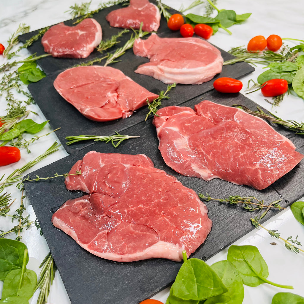 Six lamb steaks on plates with rosemary and tomatoes