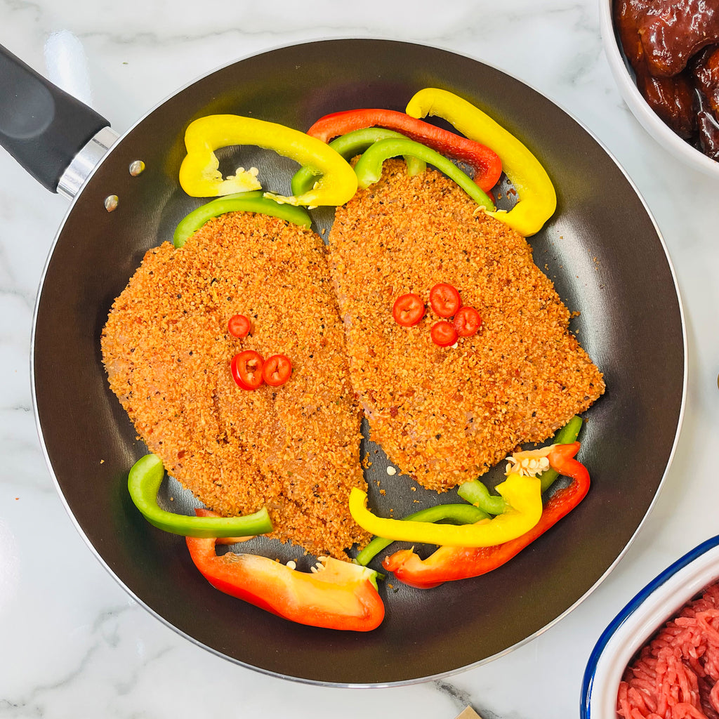 Two butterfly chicken breast fillets and peppers in a frying pan