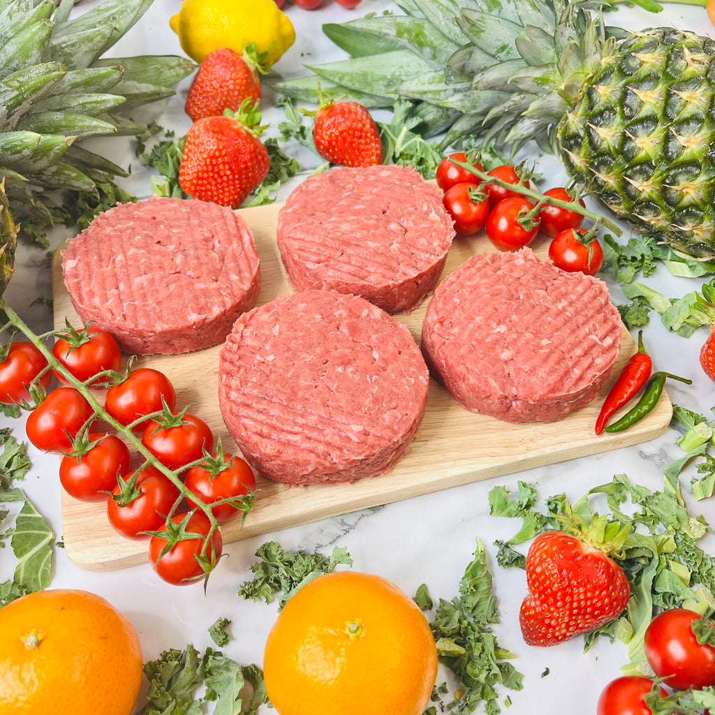 Four steak burgers on a chopping board with vegetables around