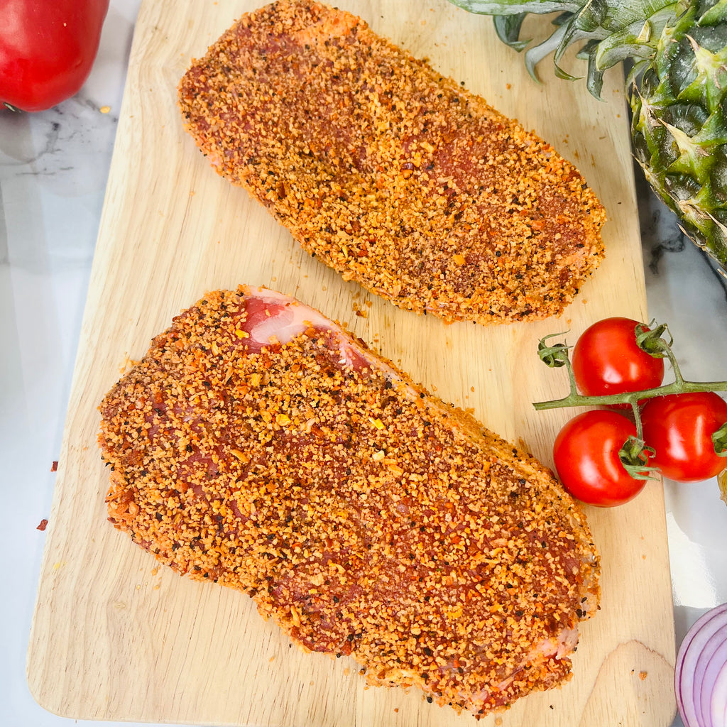 Two pepper coated tender steaks on a chopping board with tomatoes on the side