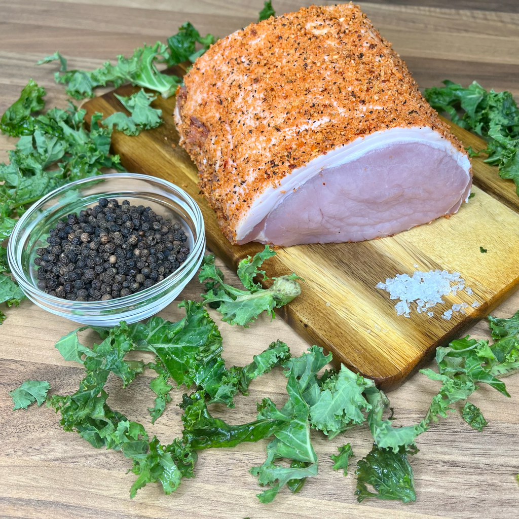 Pepper crusted pork roasting joint on a chopping board and black pepper in a bowl