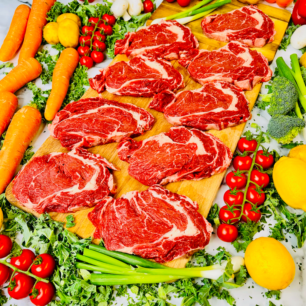 Nine fresh english ribeye steaks on a chopping board and vegetables around
